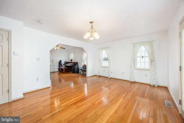 unfurnished living room featuring visible vents, arched walkways, baseboards, light wood-style flooring, and ceiling fan with notable chandelier