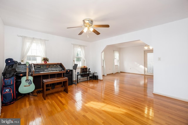 miscellaneous room featuring light wood-type flooring, ceiling fan, arched walkways, and baseboards