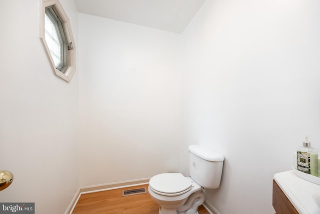 bathroom with toilet, visible vents, baseboards, and wood finished floors