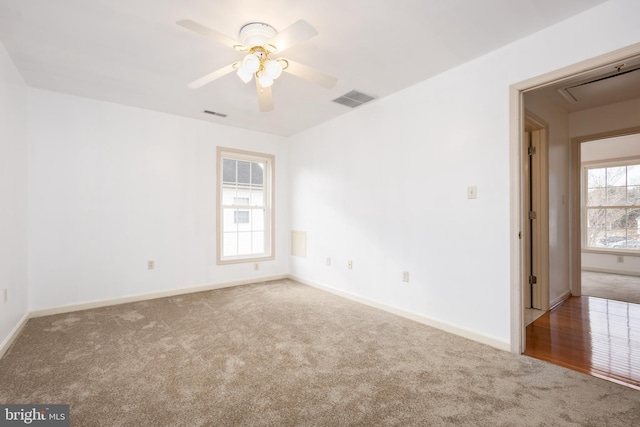 carpeted empty room with baseboards, attic access, visible vents, and a ceiling fan