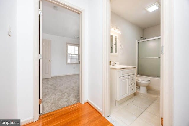 full bath featuring bath / shower combo with glass door, toilet, vanity, wood finished floors, and baseboards