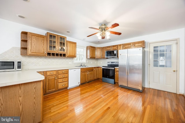 kitchen featuring brown cabinets, open shelves, decorative backsplash, appliances with stainless steel finishes, and light wood-type flooring