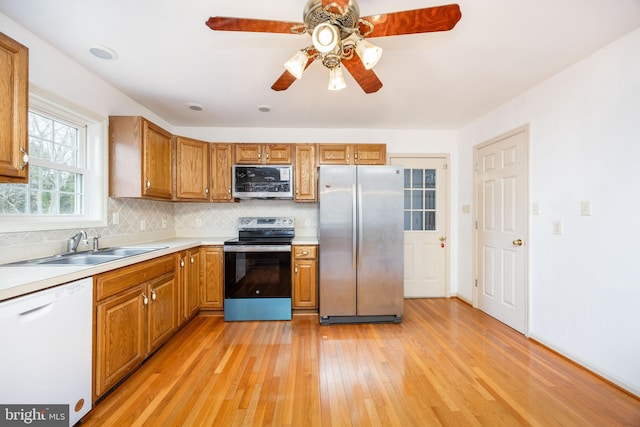 kitchen featuring stainless steel appliances, decorative backsplash, brown cabinetry, a sink, and light wood-type flooring