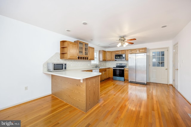 kitchen with brown cabinets, open shelves, appliances with stainless steel finishes, a sink, and a peninsula