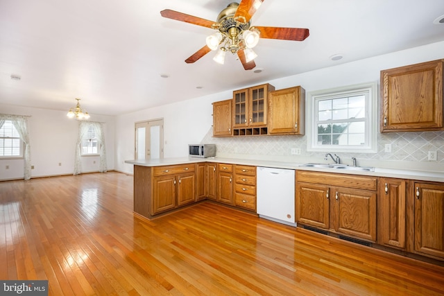 kitchen with brown cabinetry, dishwasher, stainless steel microwave, a peninsula, and a sink