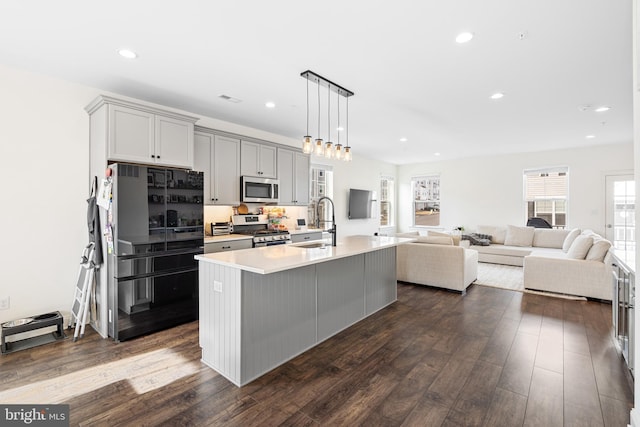 kitchen featuring an island with sink, appliances with stainless steel finishes, gray cabinets, light countertops, and a sink