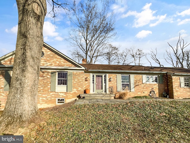 ranch-style house featuring brick siding, a chimney, and a front lawn