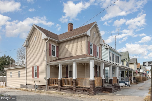 view of side of home featuring a porch, a shingled roof, and a chimney