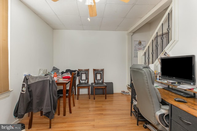 office space featuring light wood finished floors, baseboards, a ceiling fan, and a drop ceiling