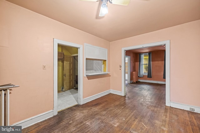 empty room featuring radiator, ceiling fan, baseboards, and wood finished floors