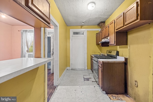 kitchen with brown cabinets, light countertops, a textured ceiling, under cabinet range hood, and stainless steel gas range oven