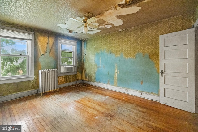 empty room featuring a ceiling fan, baseboards, radiator heating unit, wood-type flooring, and wallpapered walls