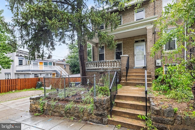 view of front of home featuring a porch, brick siding, and fence