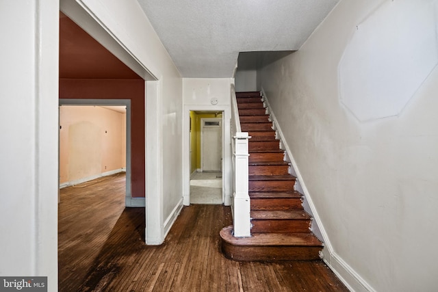 staircase featuring a textured ceiling, baseboards, and hardwood / wood-style flooring