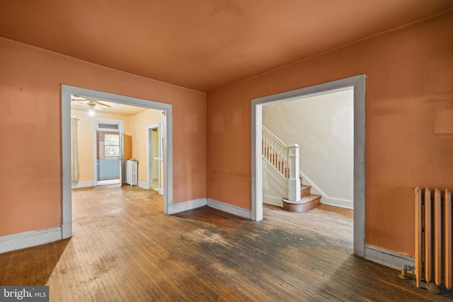 empty room featuring radiator, wood-type flooring, stairway, and baseboards