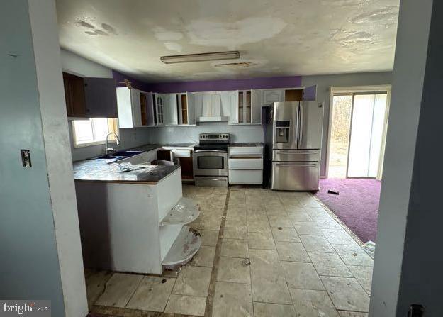 kitchen featuring stainless steel appliances, a sink, white cabinets, wall chimney exhaust hood, and glass insert cabinets