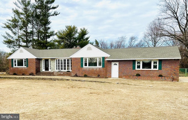 ranch-style house featuring a shingled roof, a front yard, brick siding, and a chimney