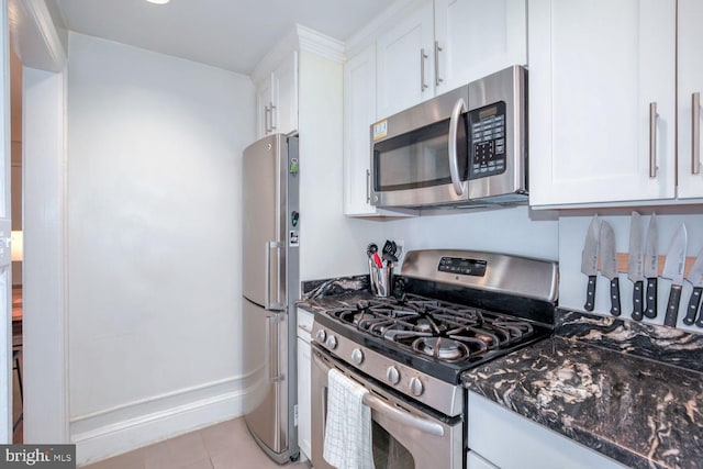 kitchen with appliances with stainless steel finishes, dark stone counters, white cabinets, and light tile patterned floors