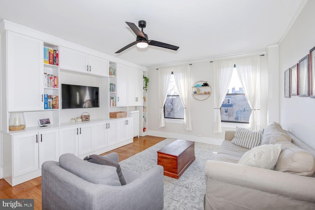 living area with ornamental molding, a ceiling fan, light wood-style flooring, and baseboards