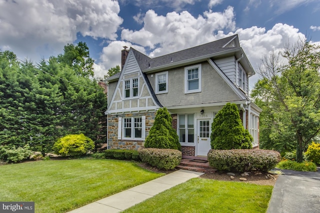 english style home with brick siding, a front lawn, stucco siding, a chimney, and stone siding