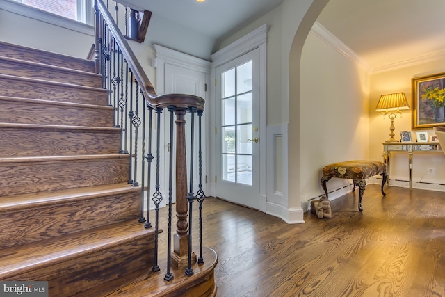 foyer with arched walkways, wood finished floors, stairs, and ornamental molding