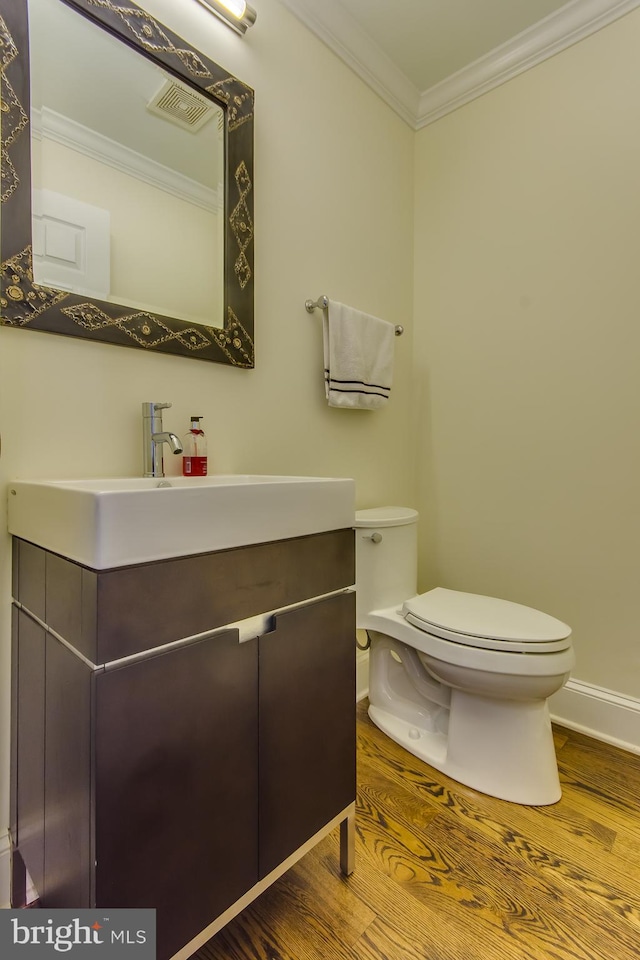 half bathroom featuring visible vents, toilet, ornamental molding, wood finished floors, and vanity