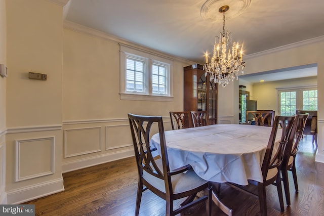 dining space featuring dark wood-style flooring, an inviting chandelier, a wainscoted wall, and ornamental molding