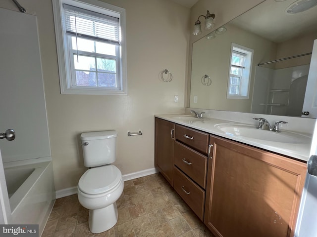 bathroom with toilet, double vanity, baseboards, and a sink