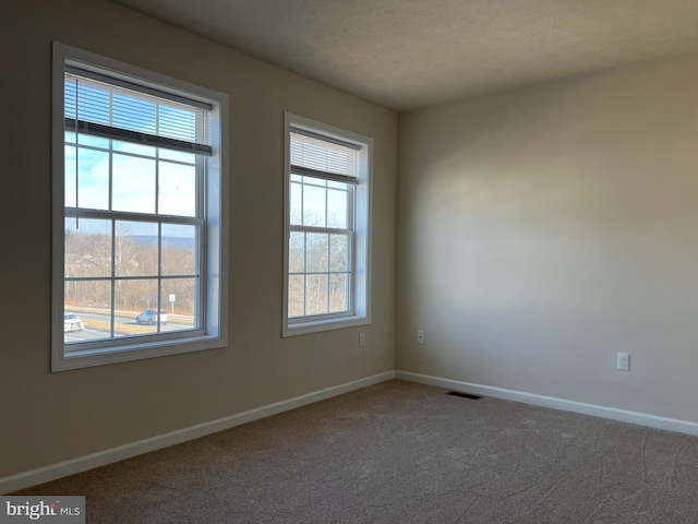 carpeted empty room with visible vents, a textured ceiling, and baseboards