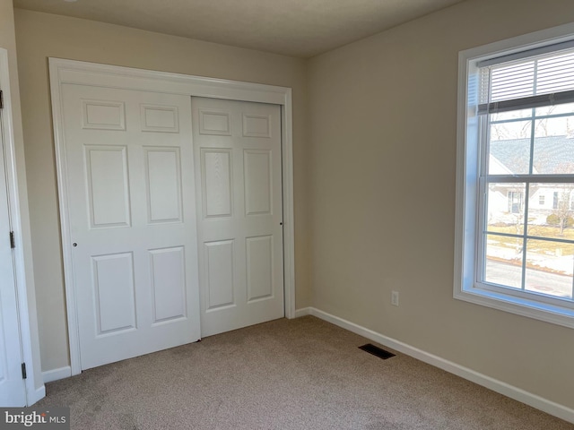 unfurnished bedroom with a closet, multiple windows, carpet flooring, and baseboards