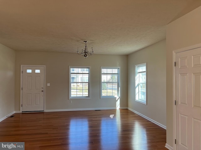 entrance foyer featuring dark wood-type flooring, a textured ceiling, baseboards, and an inviting chandelier