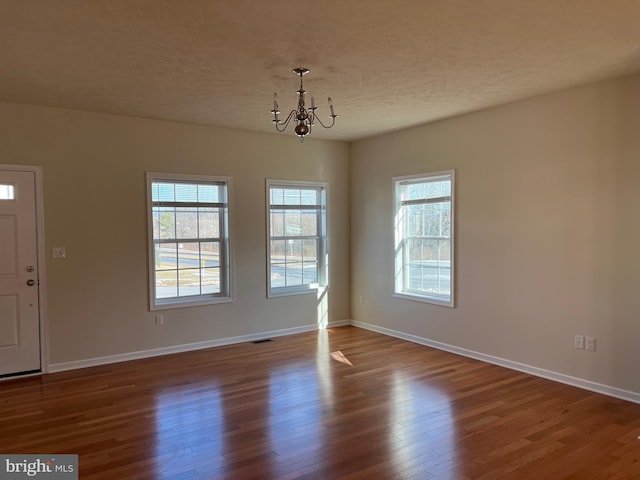 interior space featuring a chandelier, a textured ceiling, wood finished floors, visible vents, and baseboards