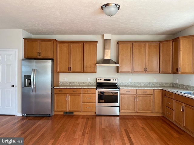 kitchen featuring light stone counters, appliances with stainless steel finishes, brown cabinets, dark wood-style flooring, and wall chimney range hood