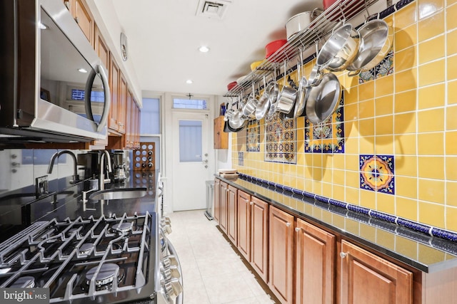 kitchen featuring light tile patterned floors, a sink, visible vents, decorative backsplash, and stainless steel microwave