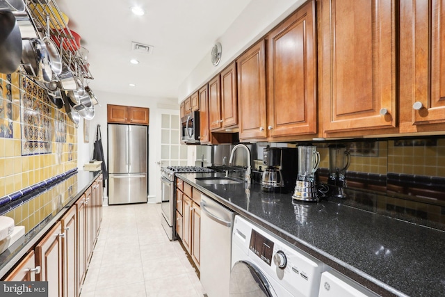 kitchen with light tile patterned floors, a sink, appliances with stainless steel finishes, decorative backsplash, and dark stone countertops