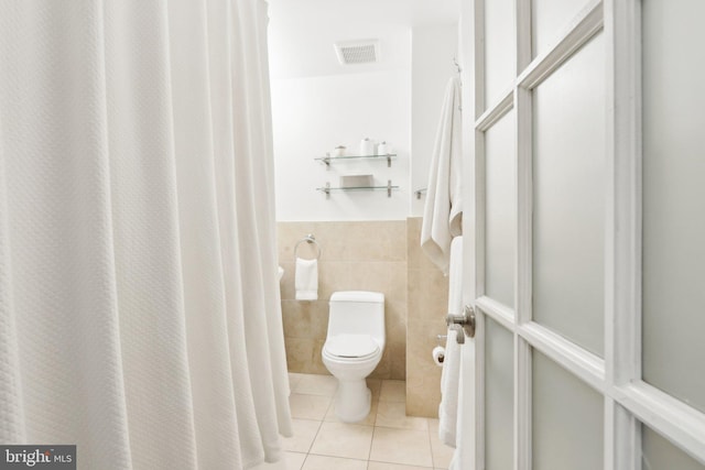 full bath with visible vents, toilet, a wainscoted wall, tile patterned floors, and tile walls