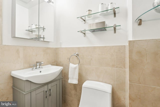 half bathroom with toilet, wainscoting, tile walls, and vanity