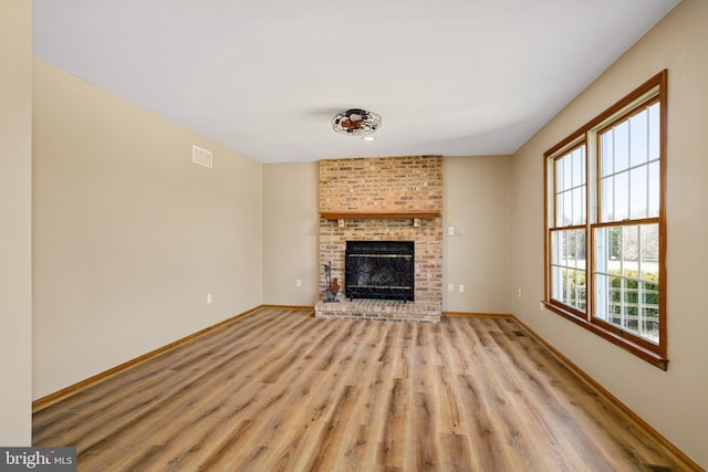 unfurnished living room with light wood finished floors, a fireplace, visible vents, and baseboards