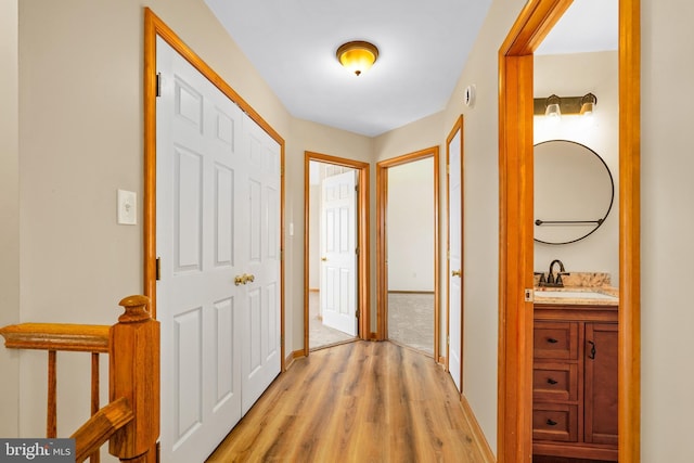 hall with light wood-type flooring, baseboards, and a sink