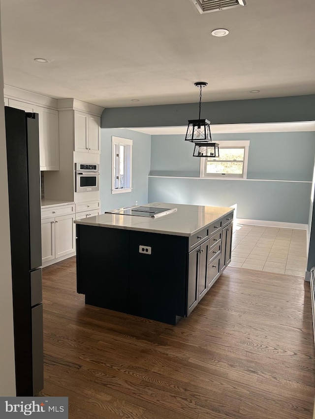 kitchen with oven, a center island, freestanding refrigerator, black electric cooktop, and light countertops