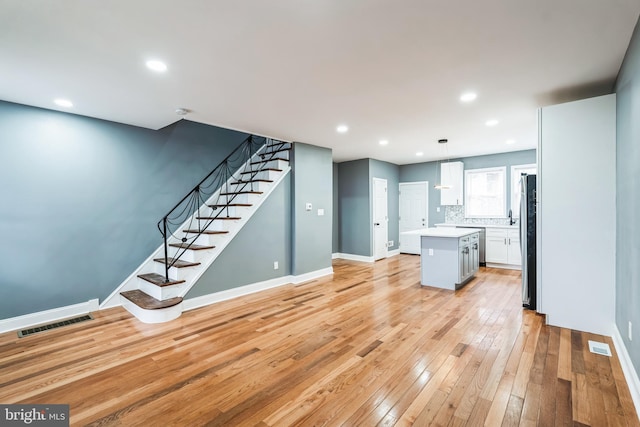 unfurnished living room with baseboards, visible vents, stairs, light wood-type flooring, and recessed lighting