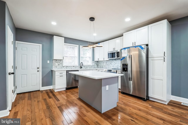 kitchen featuring appliances with stainless steel finishes, tasteful backsplash, white cabinetry, and wood finished floors