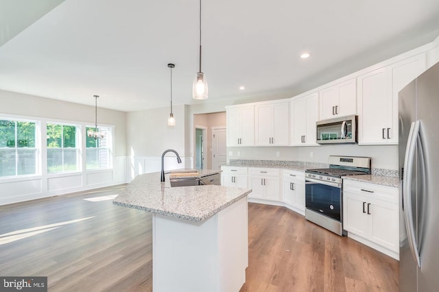 kitchen featuring stainless steel appliances, light wood-type flooring, a sink, and a center island with sink