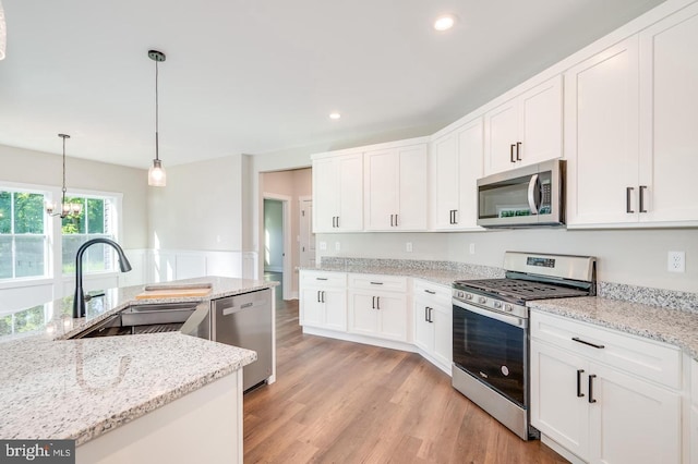 kitchen with a wainscoted wall, light wood-style flooring, appliances with stainless steel finishes, white cabinets, and a sink