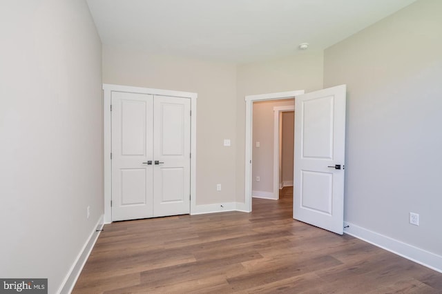 unfurnished bedroom with a closet, wood finished floors, and baseboards