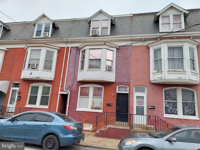 view of property featuring cooling unit, brick siding, and mansard roof