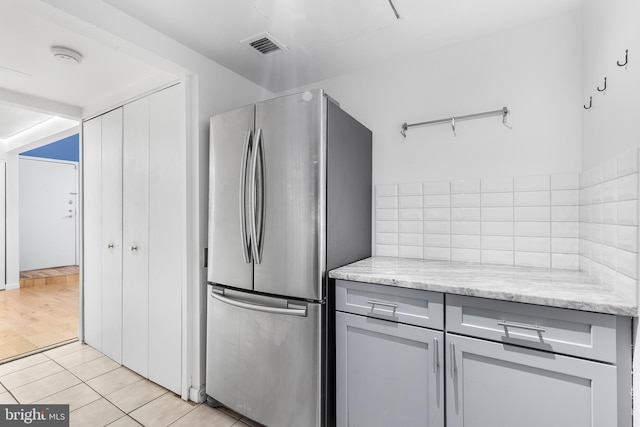 kitchen featuring light stone counters, light tile patterned floors, visible vents, gray cabinetry, and freestanding refrigerator