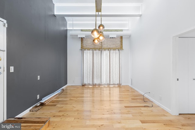 unfurnished dining area with beam ceiling, baseboards, and wood finished floors