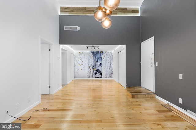 interior space with baseboards, a high ceiling, visible vents, and wood finished floors