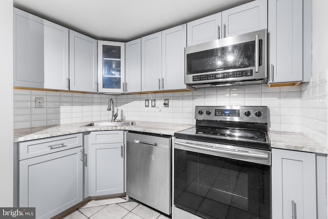 kitchen featuring decorative backsplash, light stone counters, appliances with stainless steel finishes, a sink, and light tile patterned flooring